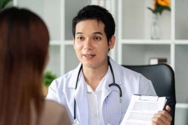 Bir doktor hastaya tedavi planını dikkatlice açıklar, destekleyici bir sağlık ortamında anlayış ve şeffaflığı teşvik eder.