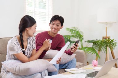 Genç bir çift, ödemelerini ve bütçelerini etkin bir şekilde planlamak için akıllı telefon ve belgelerden yararlanarak mali durumları hakkında verimli bir konuşma yapıyor..