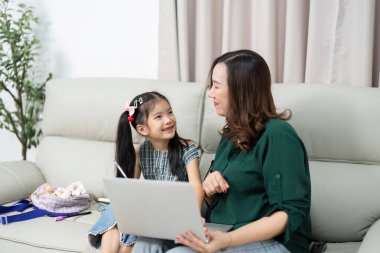 Bir anne ve kızı bir kanepede birlikte oturur ve bir dizüstü bilgisayardaki öğrenme aktivitesiyle meşgul olurlar. Bu resim okula dönüş hazırlıklarının ve aile desteğinin özünü yakalar.