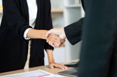 Ofis ortamında el sıkışarak iş birliği ve güveni sembolize eden iki iş adamı..