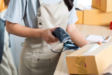 Parlak bir çalışma alanında, verimliliği ve organizasyonu somutlaştıran bir paket üzerinde barkod tarayıcısı kullanan odaklanmış bir girişimci.