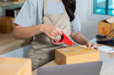 E-ticaret lojistiğinde nakliye hazırlıklarını vurgulayan bir paketi mühürlemek için bant kullanan bir girişimci.