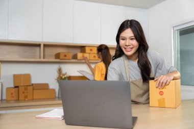 Paket tutarken gülümseyen bir girişimci ve bir dizüstü bilgisayarla müşterilerle iletişim kuran, dinamik bir iş yaklaşımı sergileyen.