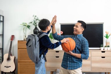 Bir baba ve oğul bir basketbol topuyla neşeyle beşlik çakıyor, evde eğlenceli ve aktif oyun zamanını sembolize ediyor..