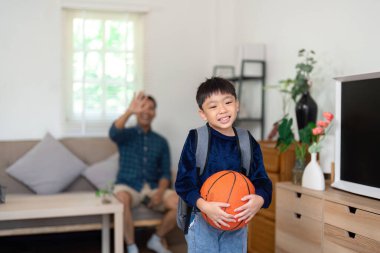 Okul için heyecanlanan genç bir çocuk, elinde bir basketbol topu tutuyor, hayatının akademik ve spor dengesini gösteriyor. Onun neşeli ifadesi yeni bir okul yılı beklentisini yansıtıyor..