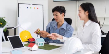 Modern bir çalışma alanında, iki mühendis, yenilikçi çözümler üretmek için ev modelleri ve rüzgar türbinleri kullanarak sürdürülebilir tasarım projeleri üzerinde işbirliği yapıyorlar..