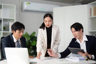 Çağdaş bir ofis ortamında çizelge ve stratejileri inceleyen, takım çalışması ve iletişimini vurgulayan çeşitli profesyoneller bir proje üzerinde işbirliği yapmaktadır..