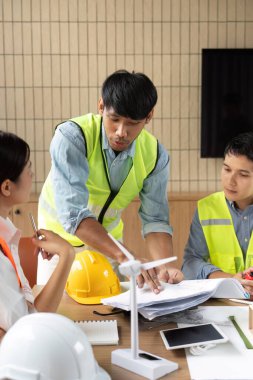 Modern bir ofiste proje planları ve sürdürülebilirlik stratejilerini tartışan bir mühendis, takım çalışmasını ve yenilikçi çözümleri vurguluyor.