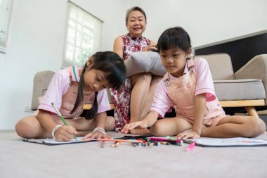 Büyükanneleri izlerken iki genç kız yerde yaratıcı çizimler yapıyor ve öğrenme ve sanatsal ifade için besleyici bir ortam yaratıyorlar..