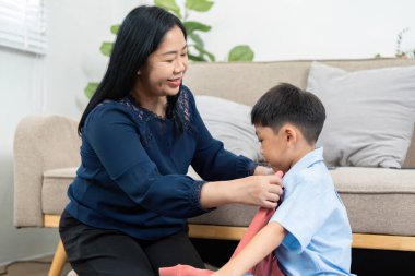 Şefkatli bir anne, oğlunun aile seyahatine hazırlanırken giydiği gömleği giymesine yardım eder. Yolculuğun heyecanı ve bağlarını vurgular..