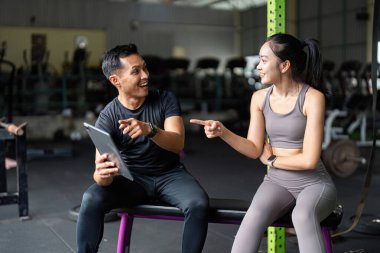 Kişisel antrenör ve müşteri, spor salonundaki fitness hedeflerini tartışarak, sağlık ve refahı teşvik ederek keyifli bir anı paylaşıyor..