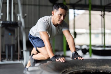 Odaklanmış bir adam zorlu bir lastik egzersizi yapıyor, dinamik bir spor salonunda güç ve kararlılık gösteriyor..