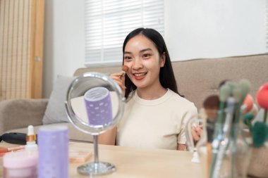 Bir kadın yanaklarına allık sürerken, makyaj rutininin son dokunuşlarından zevk alırken, neşeli ifadesini vurgularken görülüyor..