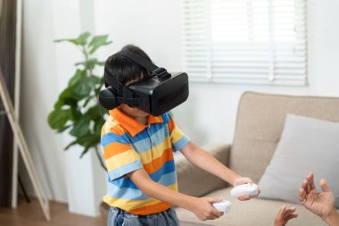 VR kulaklık takan genç bir çocuk oyun deneyiminin keyfini çıkarırken ailesi de bu zevki paylaşıyor. Teknoloji sayesinde aile bağlarının neşesini sergiliyor..