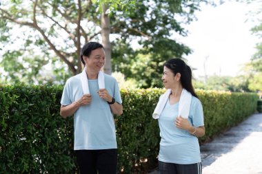 Üst düzey bir çift parkta yan yana yürür, birlikte sağlıklı bir hayat sürerken gülümsemelerini ve gülüşmelerini paylaşırlar..