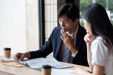 İki profesyonel iş danışmanlığı yapıyor, belgeleri analiz ediyor ve modern ofis ortamında stratejileri tartışıyorlar..