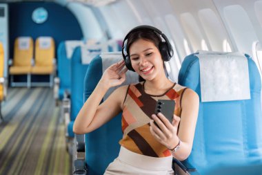 Neşeli bir turist, bir uçakta modern bir seyahat deneyimi sergileyerek, kulaklıklarıyla eğlenmeyi sever..