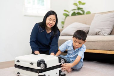 Anne ve oğlu toplanan bavullarını kapatmak için işbirliği yapıyorlar. Aile gezisine hazır olduklarını ve ortak deneyimlerin keyfini simgeliyorlar..