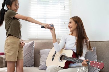 İki kız bir mikrofon ve gitarı paylaşıyor, eğlenceli bir müzik deneyimini teşvik ediyor ve sıcak bir oturma odasında arkadaşlıklarını sergiliyorlar..