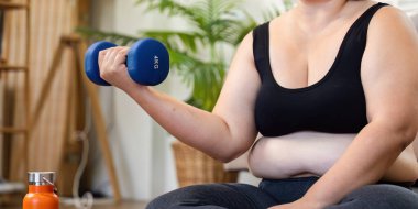 Kararlı bir kadın, konforlu bir ev ortamında refahı ve zindeliği arttırmak için halterini kaldırarak güç egzersizi yapar..