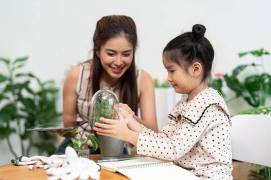 Neşeli bir anne-kız bağ kurarken kapalı bir bahçede bitkileri besliyor, sürdürülebilirliği ve aile bağlarını destekliyor..
