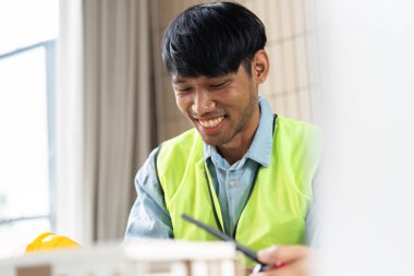 Güvenlik yeleği giyen bir mühendis sürdürülebilir tasarım oturumunda gülümsüyor, yeşil teknoloji projelerine karşı coşku ve kararlılık gösteriyor.