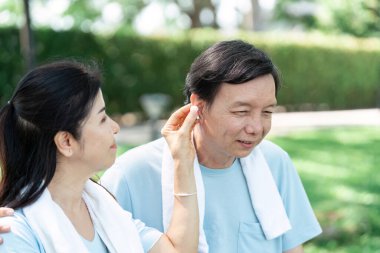 Bir kadın, açık havada güneşli bir günün tadını çıkarırken ortağına kulaklık takmasında yardım eder. Bağlantının altını çizer ve aktivitelerini paylaşır..