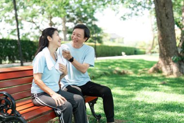 Yaşlı bir çift yemyeşil bir parkta bankta oturuyor, neşeli bir anı paylaşıyor ve kahkaha ve şefkat ile bağlarını güçlendiriyor..