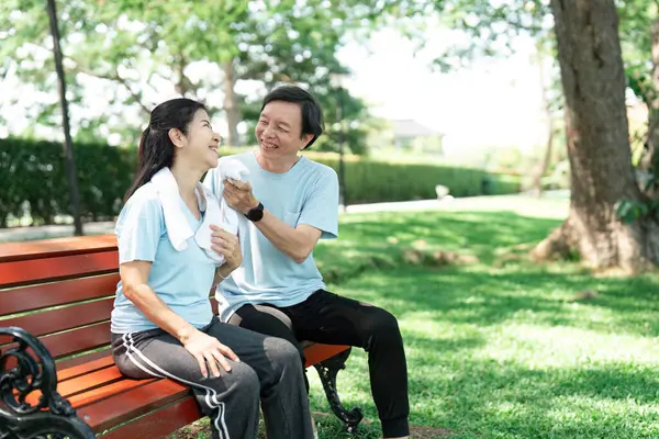 Yaşlı bir çift yemyeşil bir parkta bankta oturuyor, neşeli bir anı paylaşıyor ve kahkaha ve şefkat ile bağlarını güçlendiriyor..