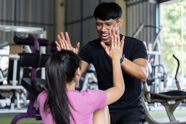 Kişisel antrenör, kadın müşteriyi spor yaparken hevesle teşvik eder ve destekleyici bir spor salonu ortamı sağlar..