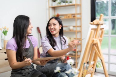 İki arkadaş neşeli bir resim seansına katıldı. Parlak bir odada gülüşmeler ve sanatsal ifadelerle dolu..