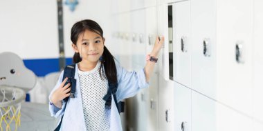 Sırt çantalı neşeli bir liseli kız dolapların yanında duruyor. Okula geri dönmenin ve yeni başlangıçların heyecanını simgeliyor..