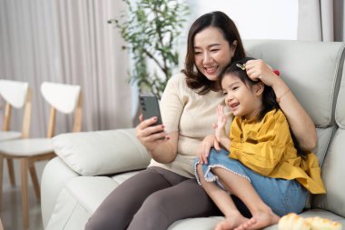 Bir anne ve kızı görüntülü konuşma yaparken gülücüklerini paylaşıyor, oturma odasında mutlu anılar yaratıyorlar..