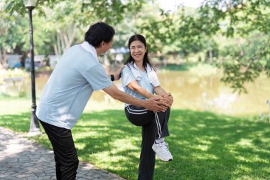 Yaşlı bir adam huzur parkında egzersiz rutininde bir kadına yardım ediyor. Kıdemli fitness ve aktif yaşam tarzını vurguluyor..