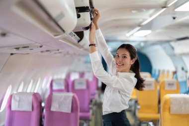 İş seyahati sırasında bavullarını bir uçağın tepesindeki kutuya koyarken gülümseyen genç bir kadın..