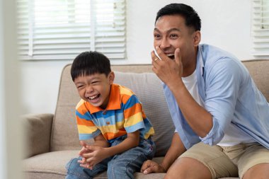 Bir baba ve oğul birlikte neşeli anlarını vurgulayan bir video oyunu izlerken kahkahalarını paylaşırlar..