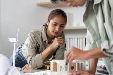 İki mimar sürdürülebilir bir yapı modelini tartışıyor, çevre dostu bir çalışma alanında takım çalışması ve yenilikçi tasarımı vurguluyor.