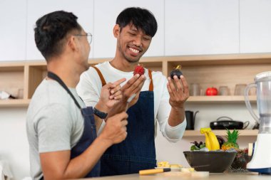 Önlüklü iki neşeli adam birlikte taze meyveler hazırlıyor, canlı bir mutfakta aşk ve aşçılık yaratıcılığını kutluyorlar..