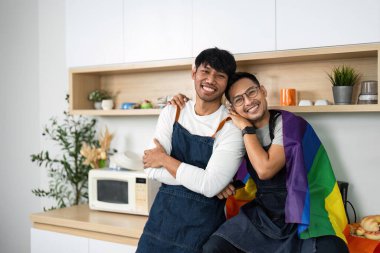 İki adam mutlulukla poz veriyor. Gökkuşağı bayraklarıyla modern mutfaklarında. Aşkı ve kapsayıcılığı temsil ediyorlar..