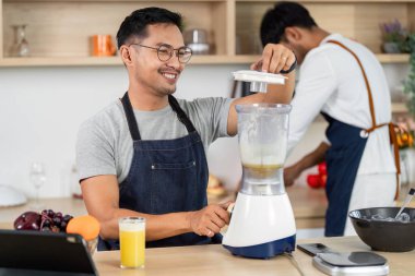 Bir adam malzemeleri harmanlarken, diğer bir saat modern bir mutfakta takım çalışması ve neşe sergiliyor..