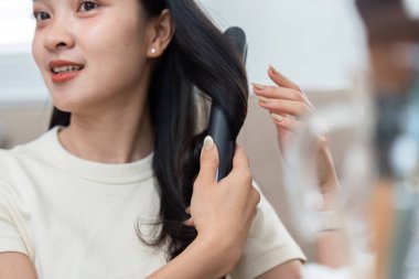 Bir kadın saçlarını kıvırtır, güzellik rutinini gösterir. Görüntü, saç modellemesinin genel görünümü geliştirmedeki önemini vurgular..