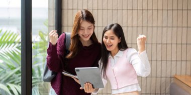 İki öğrenci akademik başarılarını neşeyle kutluyor. Sonuçlarını heyecanlı bir şekilde tablet üzerinde gözden geçiriyorlar..