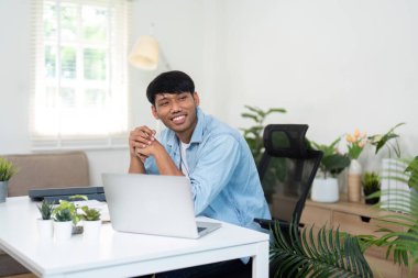 Genç bir profesyonel ofis masasına gülümsüyor, uzak iş ve iş memnuniyetine karşı olumlu bir tavır sergiliyor..