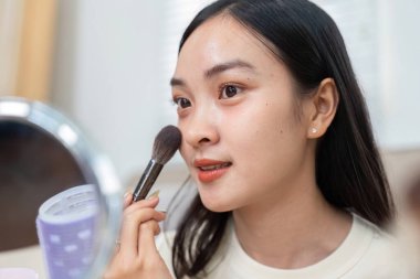 Bir kadın yüzüne bir fırçayla bronzlaştırıcı sürüyor, güzellik rejiminin bir parçası olarak özelliklerini geliştirmeye odaklanıyor..