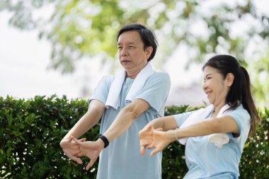 Üst düzey bir çift, sakin bir açık hava ortamında esneme egzersizleri yapıyor, birlikte sağlık ve fiziksel zindelik üzerine odaklanıyorlar. Bağlantıları aktif kalmanın önemini vurguluyor.