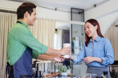 Dost canlısı bir kafede sürdürülebilir uygulamaları vurgulayarak, bir barista memnun bir müşteriye kahve verir..