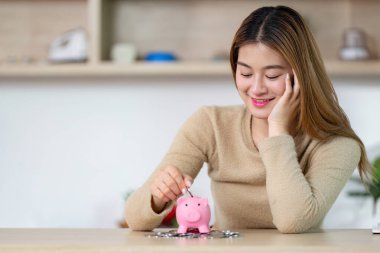 Genç bir kadın, para biriktirme sürecinden zevk alıyor. Paraları kumbaraya yerleştirirken finansal hedeflerini de göz önüne alıyor..