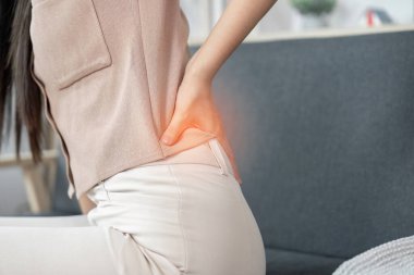 Koltukta oturan genç bir kadın, sırt ağrısı çekiyor, fiziksel sağlığın ve kendine bakmanın önemini vurguluyor..