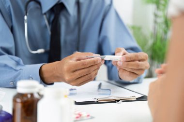 Bir sağlık hizmeti sağlayıcısı, profesyonel bir tıbbi muayenede hastanın sıcaklığını ölçmek için termometre tutar..