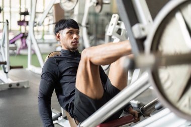 Genç bir adam spor salonunda bacak egzersizi yapmaya odaklanır. Güç gösterisi ve kendini adamışlık gösterir..